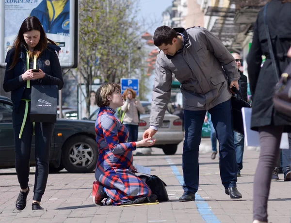 Hamile bir kadın kaldırımda diz çöküp yalvarıyor, erkek ona bozukluk veriyor. 10 Ekim 2019. Kiev, Ukrayna