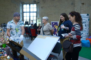 Ressam, basım ürünlerini izleyen müşterilere sunarken albümünü ters çeviriyor. Kitap Fuarı Knyzhkovyi Arsenal. 24 Mayıs 2019. Kiev, Ukrayna