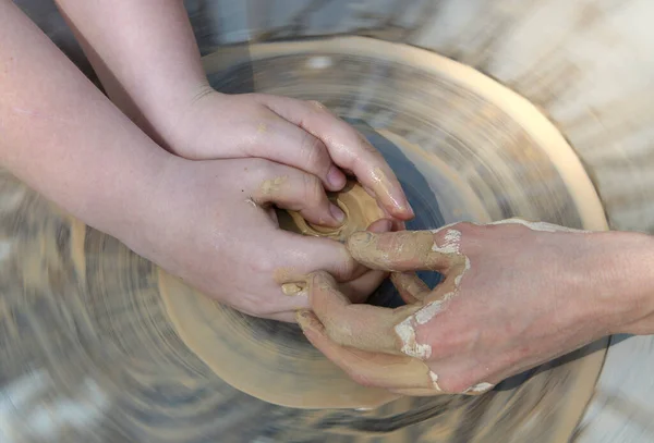 Teaching of wheel throwing. Potter s hand correcting child s ones during shaping clay blank on a potter\'s wheel