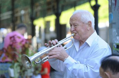 Sokakta trompet çalan yaşlı bir adam, arka planda yürüyen insanlar.