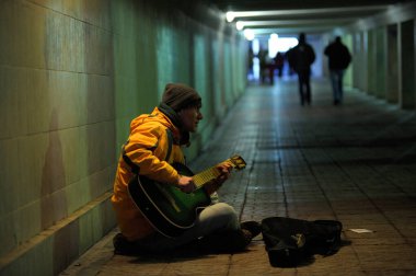 Busker metroda kaldırımda oturur ve gitar çalar, arka planda yürüyen bulanık yayalar. 26 Ekim 2019. Kiev, Ukrayna