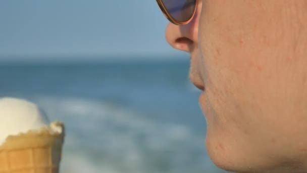 Jovem morena lambendo comer gelado na praia, fundo azul do mar e óculos de sol . — Vídeo de Stock