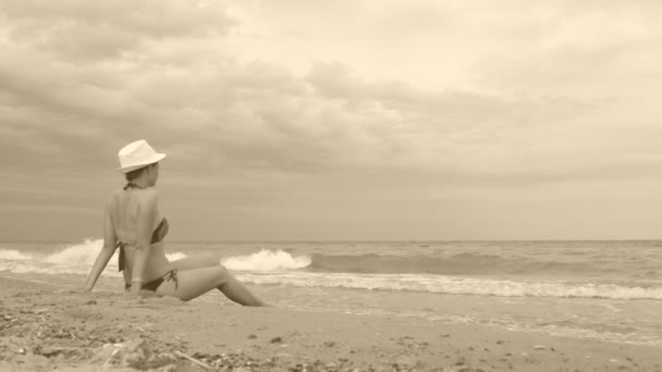 La ragazza in cappello bianco siede sulla riva del mare durante una piccola tempesta . — Video Stock