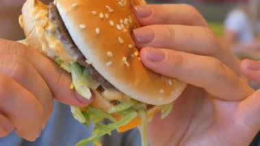 Hamburger yiyen bir kız. Yakın plan çekim. Fast food yer. Hamburger kadınların elinde..