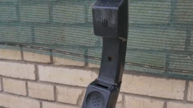 Duvarın yanında asılı duran eski bir ankesörlü telefon ahizesi.