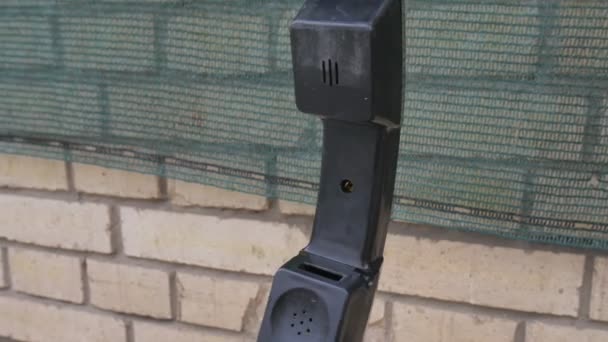 Old pay phone handset dangling next to tile brick wall — Stock Video