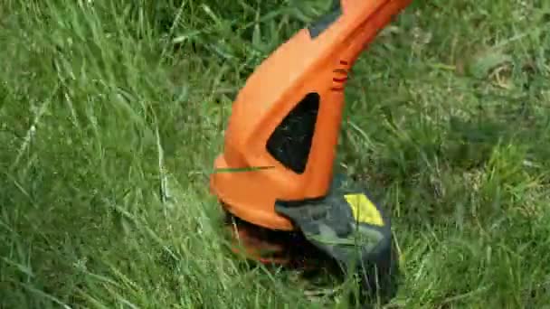 Moderner elektrischer orangefarbener Trimmer mit schwarzen Details mäht grünes Gras. Nahaufnahme. — Stockvideo
