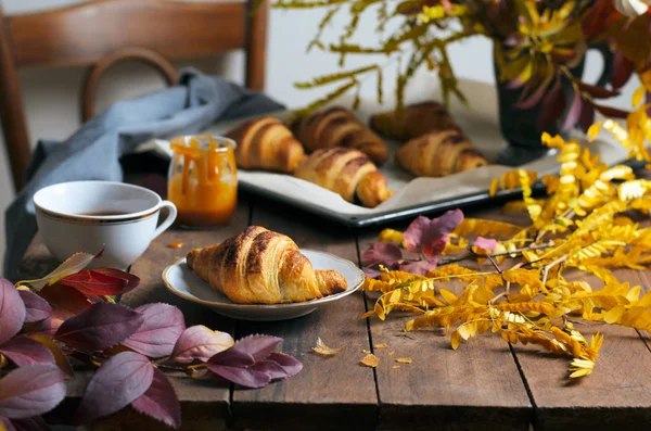 Cozy Autumn Still Life, Fall Breakfast, Freshly Baked Croissants with Cinnamon and Salted Caramel, Cup of Tea and Autumn Leaves on Wooden Table