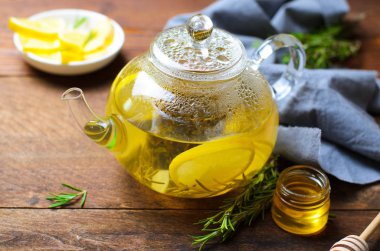 Limonlu sağlıklı zencefil çay, biberiye ve koyu ahşap arka plan üzerinde cam çaydanlık bal