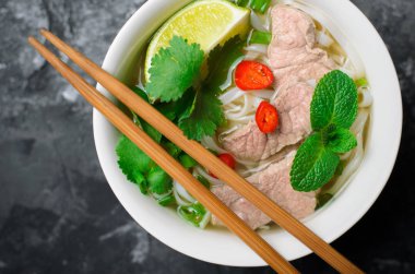 Geleneksel Vietnam çorba Pho Bo pirinç noodle, sığır eti ve otlar üzerinde koyu arka plan, Asya mutfağı