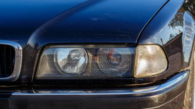 Güneşli bir yaz gününde, tuğladan bir kaldırıma park etmiş siyah bir Alman arabası. Arka planda yeşil ağaçlar var.