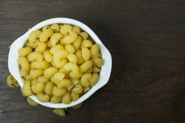 Ahşap masa üzerinde beyaz kase pişmemiş makarna