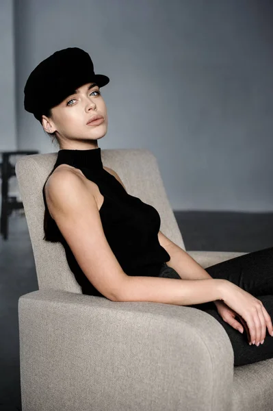 Brunett flicka i svart med mössa poseras på studio på stol — Stockfoto