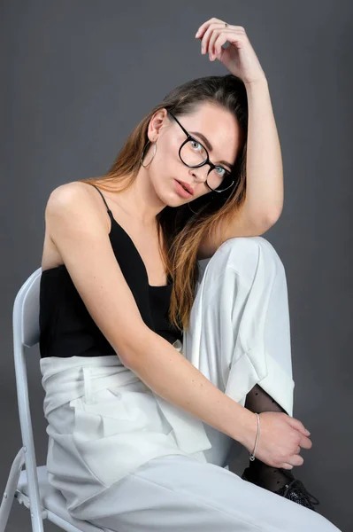 Méditer fille dans des lunettes, s'assoit sur la chaise sur fond gris — Photo