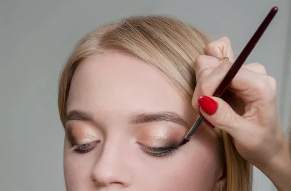 Make-up kunstenaar werken in make-up Studio, past een borstel op het ooglid. op blonde gezicht — Stockfoto