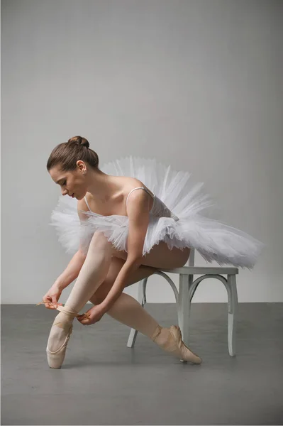Bailarina em um vestido branco sentado em uma cadeira e amarrando sua bola — Fotografia de Stock