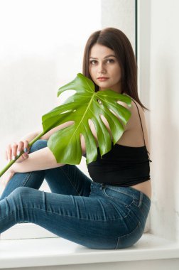 Kot pantolonlu kız elinde monstera bir yaprak ile.