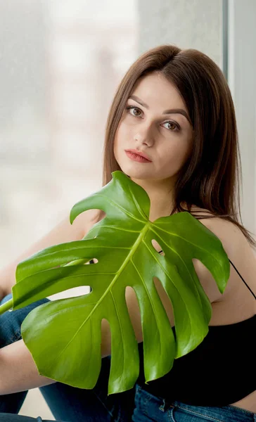 La fille en jean est avec une feuille de monstera dans ses mains . — Photo