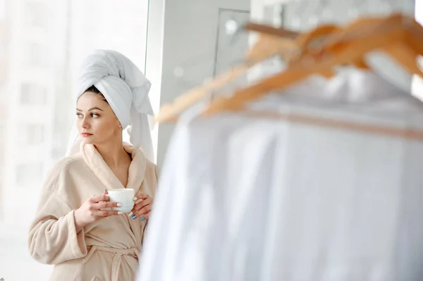 Retrato chica con toalla en la cabeza cerca de la ventana con una taza de cofee, concepto de relajación de estilo casero después de la ducha . —  Fotos de Stock