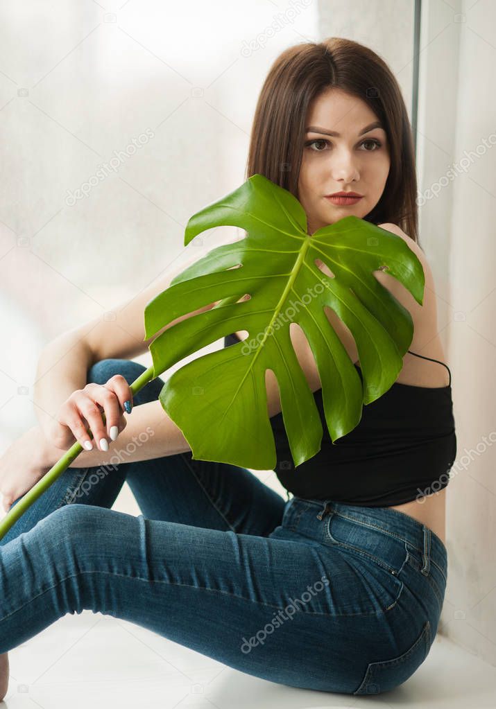 The girl in jeans is with a leaf of monstera in her hands.