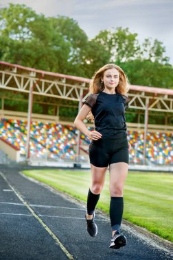 Genç, sportif kız stadyumda koşuyor.