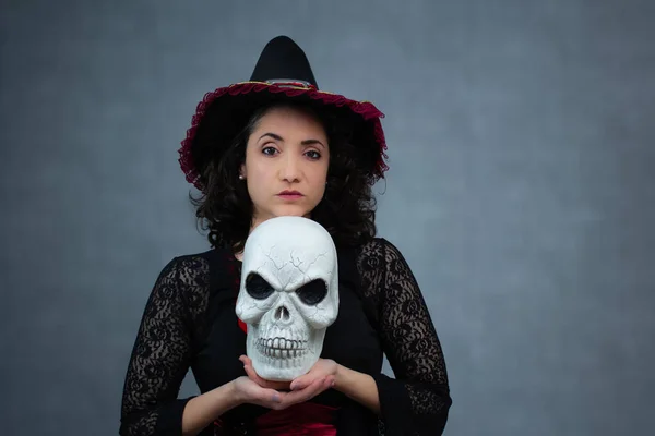 Güçlü ve küstah cadı kaşlarını kaldırmış çenesinin altında bir kafatası tutuyor. Cadılar Bayramı için ideal, peri masalı kötü adamı ve kara büyü. Geniş kopya alanına sahip yatay stüdyo portresi.