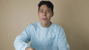 Kahverengi derili latin genç, pastel mavisi kazaklı açık kahverengi arka planda enerjik cesaret verici bir jest yapıyor motivasyon kavramı, pozitiflik, gençlik tarzı.