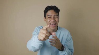 Koyu tenli, mavi kapüşonlu, biriyle alay ederken gülen genç bir Latin adamın videosu. Şakacı bir ifadeyle alay etme, mizah ve alaycı kahkaha kavramı.