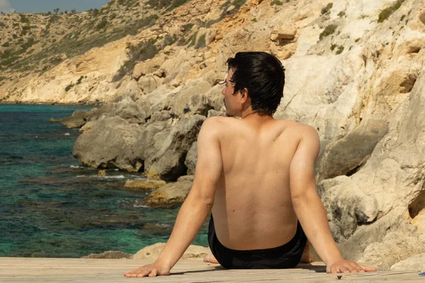 Yüzme, güneşlenme ve doğal manzarayı gözlemleme, rahatlama, tatil, turizm ve doğa ile bağlantı kurma kavramından sonra bir sahil yolunda oturan adam.