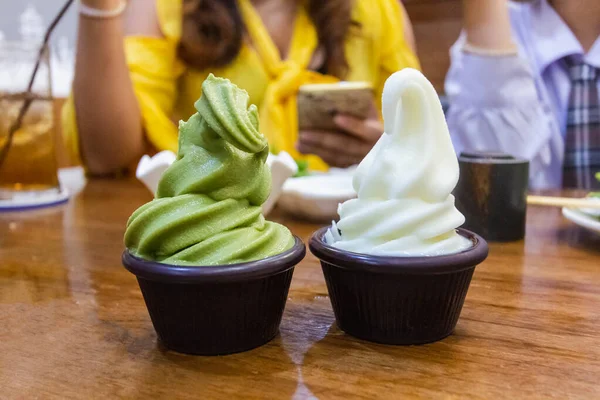 Green tea and milk ice cream in cup put on wood table at restaurant with people background