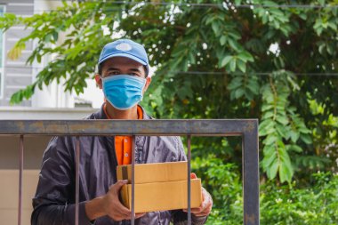 Asyalı teslimatçı iki eliyle posta kutusunu kameraya bakarak müşteriye uzatıyor.