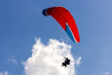 Beyaz bulutun arasında yüzen kırmızı paraşütli tandem yamaç paraşütü