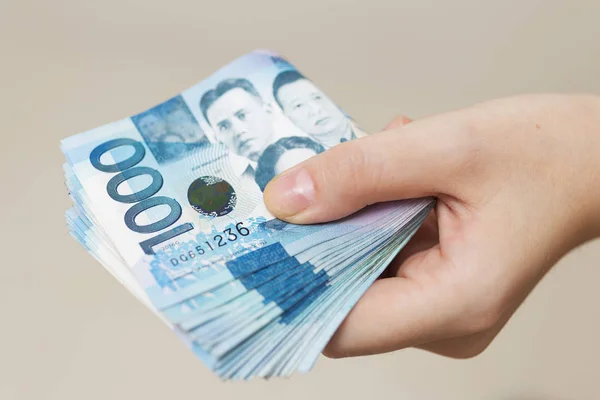Hand holding folded bundle of blue money in cash of one thousand Philippines peso. Giving bribe, paying bills or getting salary. Payment day!