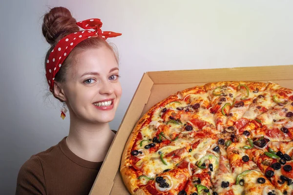 Kocaman bir aile büyüklüğünde pizzayı elinde tutan gülümseyen beyaz bir kadın. Yiyecek teslimatı kavramı