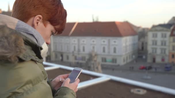 Vacker kvinna skickar ett textmeddelande med en app på sin smartphone medan du sitter på en strandpromenad i centrum — Stockvideo