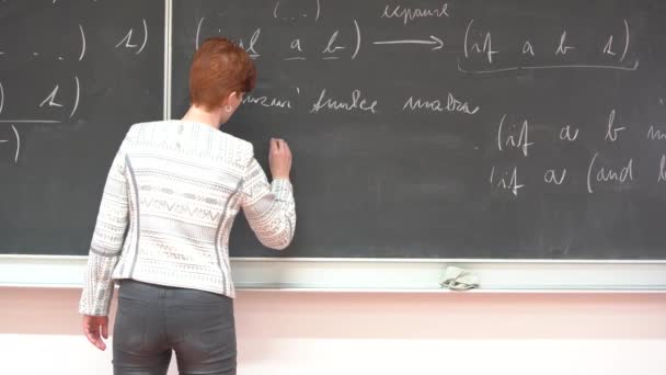 Ung kvinnlig lärare skriver på svarta tavlan matematisk formel med krita — Stockvideo