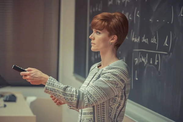 Young woman teacher in college. Instruction in a university classroom. Blackboard described by chalk. Projection from the data projector — Stock Photo, Image