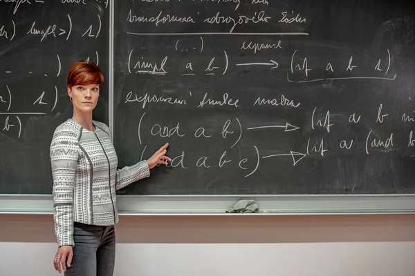 Ung kvinna lärare i College. Undervisning i ett universitets klassrum. Blackboard beskrivs av krita. Projicering från dataprojektorn — Stockfoto