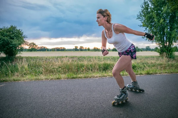 young woman rides on roller skates on an asphalt trail outside the city in summer