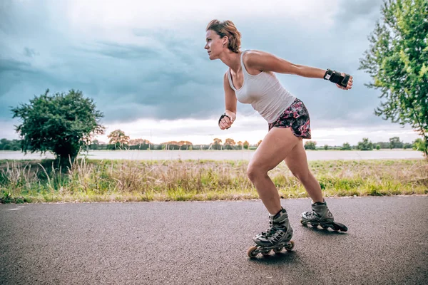 young woman rides on roller skates on an asphalt trail outside the city in summer