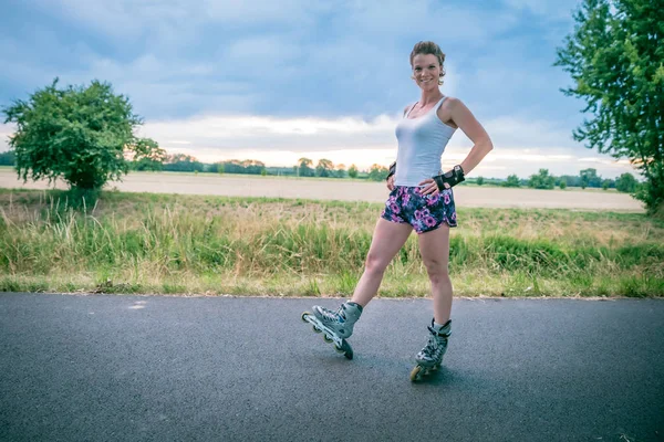 young woman rides on roller skates on an asphalt trail outside the city in summer