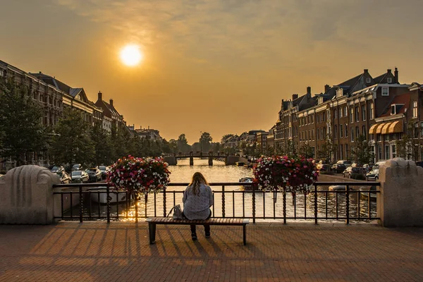 Zonsopgang over een kanaal bij een windmolen in Nederland Amsterdam. Een eenzame vrouw op een bank op een brug — Stockfoto