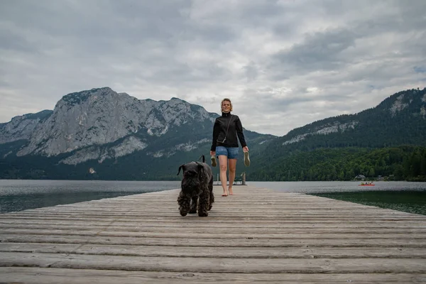 Jonge vrouw met haar hond genieten van de sfeer van een bergmeer op de pier — Stockfoto