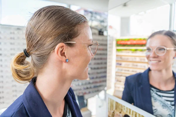 Mujer de negocios intenta gafas delante de un espejo en una tienda de óptica — Foto de Stock