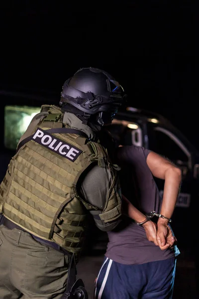Поліцейський під час арешту кладе наручники на руки злочинців. Поліцейський автомобіль з блимаючими маяками. Розмиті — стокове фото