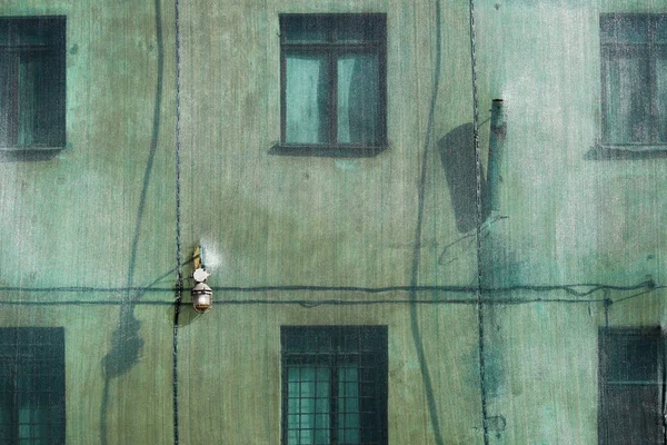 The green building mesh on old house with windows protects the old historical building from destruction and pedestrians from the shedding of plaster, drain pipe and the old lantern. — Stock Photo, Image