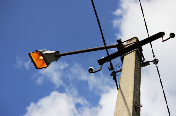 один городской фонарь на бетонной колонне зажег летний солнечный день на фоне голубого неба
