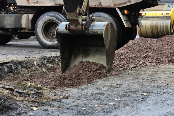 Tractor fuerte outrigger piernas estabilizadoras extendidas para estabilizar y estado estable al cavar el suelo antes de aplicar un parche de asfalto en una parte de la carretera durante la reparación — Foto de Stock