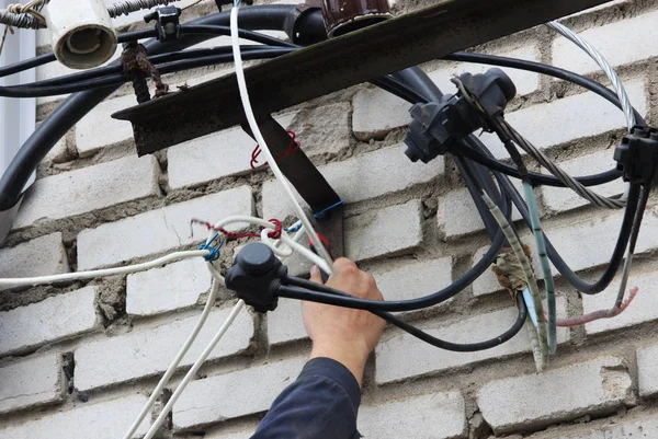 Elektryk z brygady odłącza kabel z którego czerwone światła ostrzegawcze na ogrodzeniu naprawy były karmione podczas eliminacji awarii w elektrowni wodnej. Reportażowa fotografia — Zdjęcie stockowe