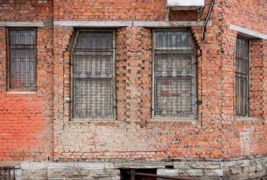 Metal bir ızgarayla korunan dikdörtgen pencereli kırmızı tuğlalı bir bina. Gatchina, Rusya.